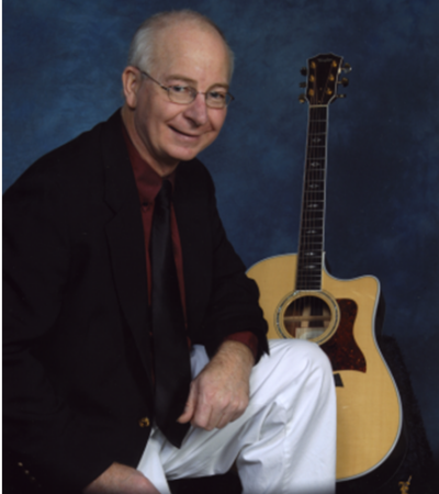 Larry Miller, sitting in front of a guitar with a blue background